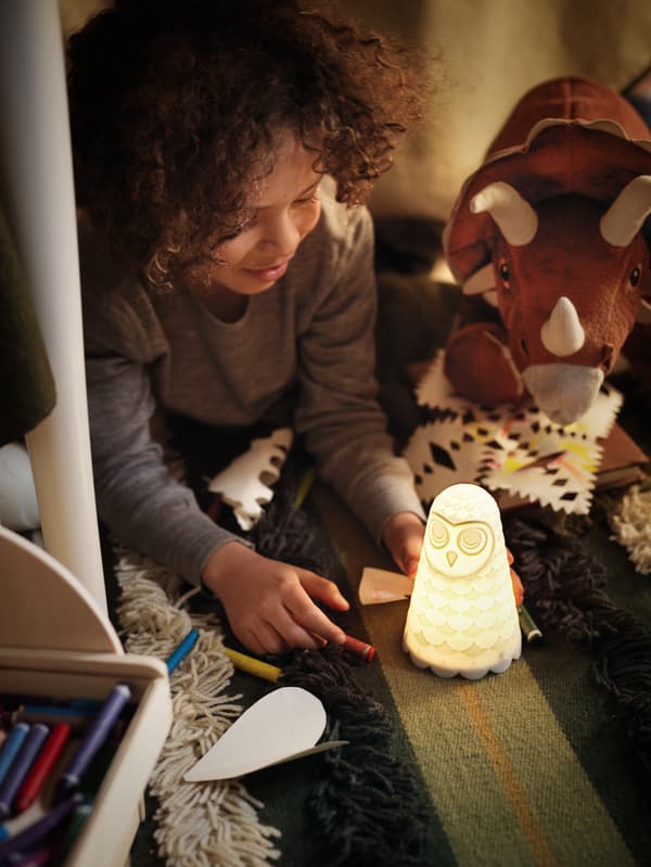 Under a table, a boy plays with a SOLBO night light that illuminates his face and his toy dinosaurs.