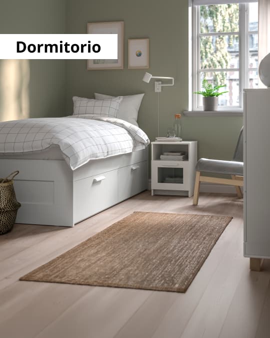 Undormitorio con cama con cajones, un velador pequeño y una alfombra IKEA como bajada de cama.