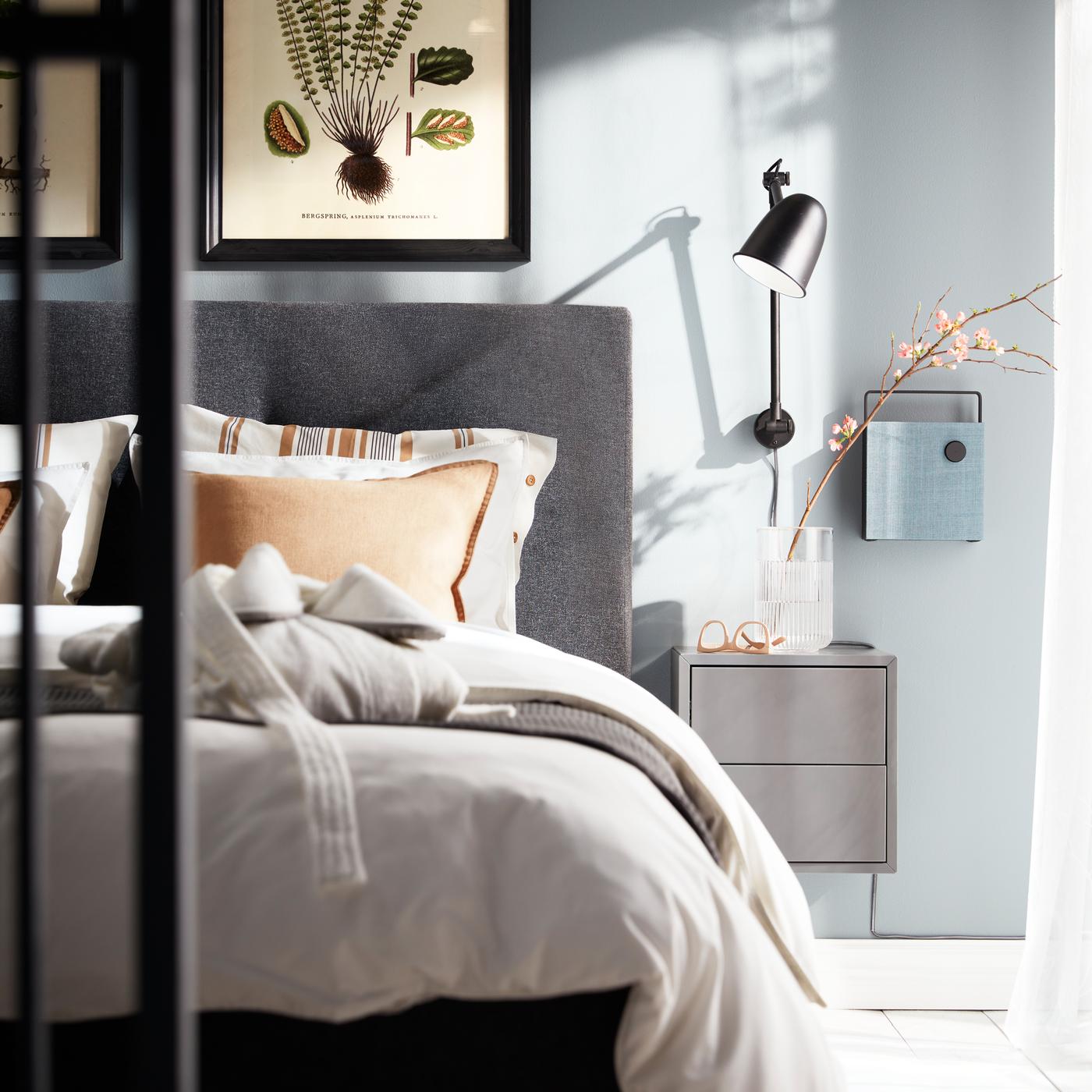 Une applique murale SKURUP, un élément EKET gris foncé et une enceinte Bluetooth fixée au mur à côté d’un lit IDANÄS gris foncé.