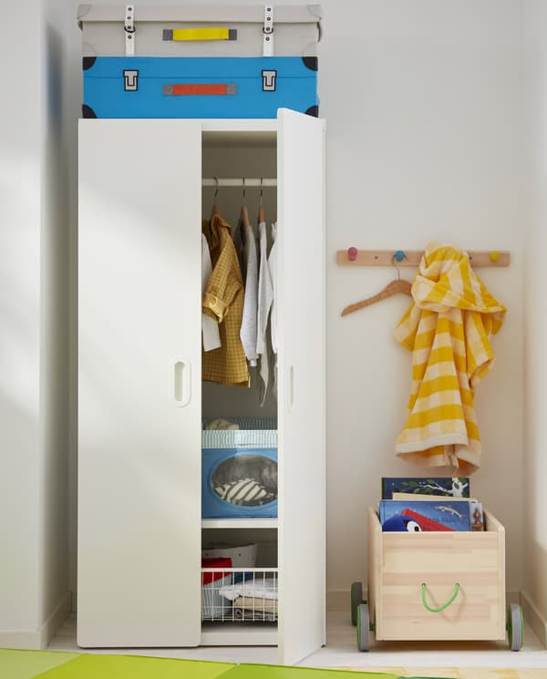 Une armoire STUVA/FRITIDES avec des vêtements rangés à l’intérieur. À côté: une patère à boutons et un rangement de jouets FLISAT.