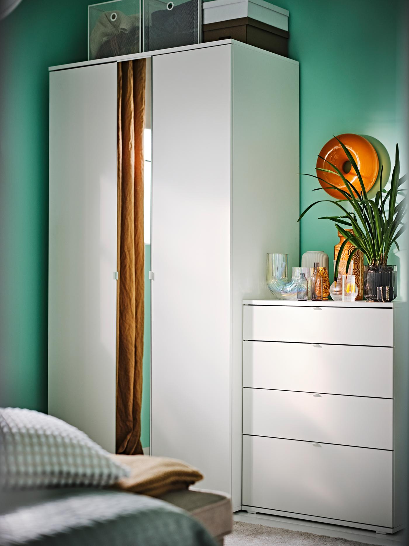 Une armoire VIHALS blanche à 2 portes à côté d’une commode 4 tiroirs VIHALS blanche dans une chambre aux murs verts.