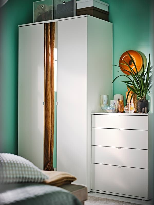 Une armoire VIHALS blanche à 2 portes à côté d’une commode 4 tiroirs VIHALS blanche dans une chambre aux murs verts.