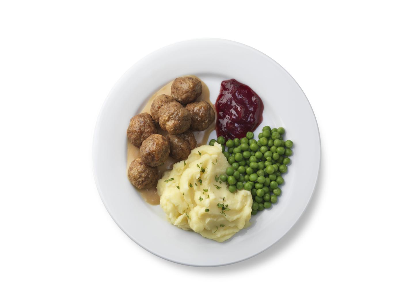 Une assiette blanche avec de la purée de pommes de terre, des petits pois et des boulettes de viande nappées de sauce.