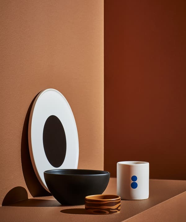 Une assiette blanche avec un centre noir, un grand bol noir, un petit bol brun et une tasse blanche sur une marche orange.