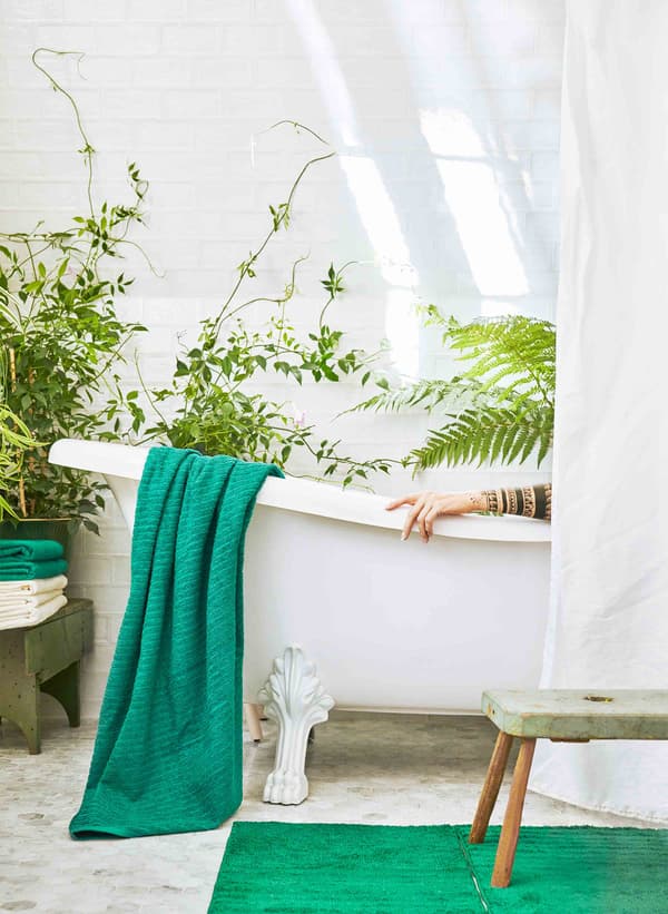 Une baignoire blanche dans une salle de bain remplie de plantes vertes, à moitié cachée par un rideau blanc.
