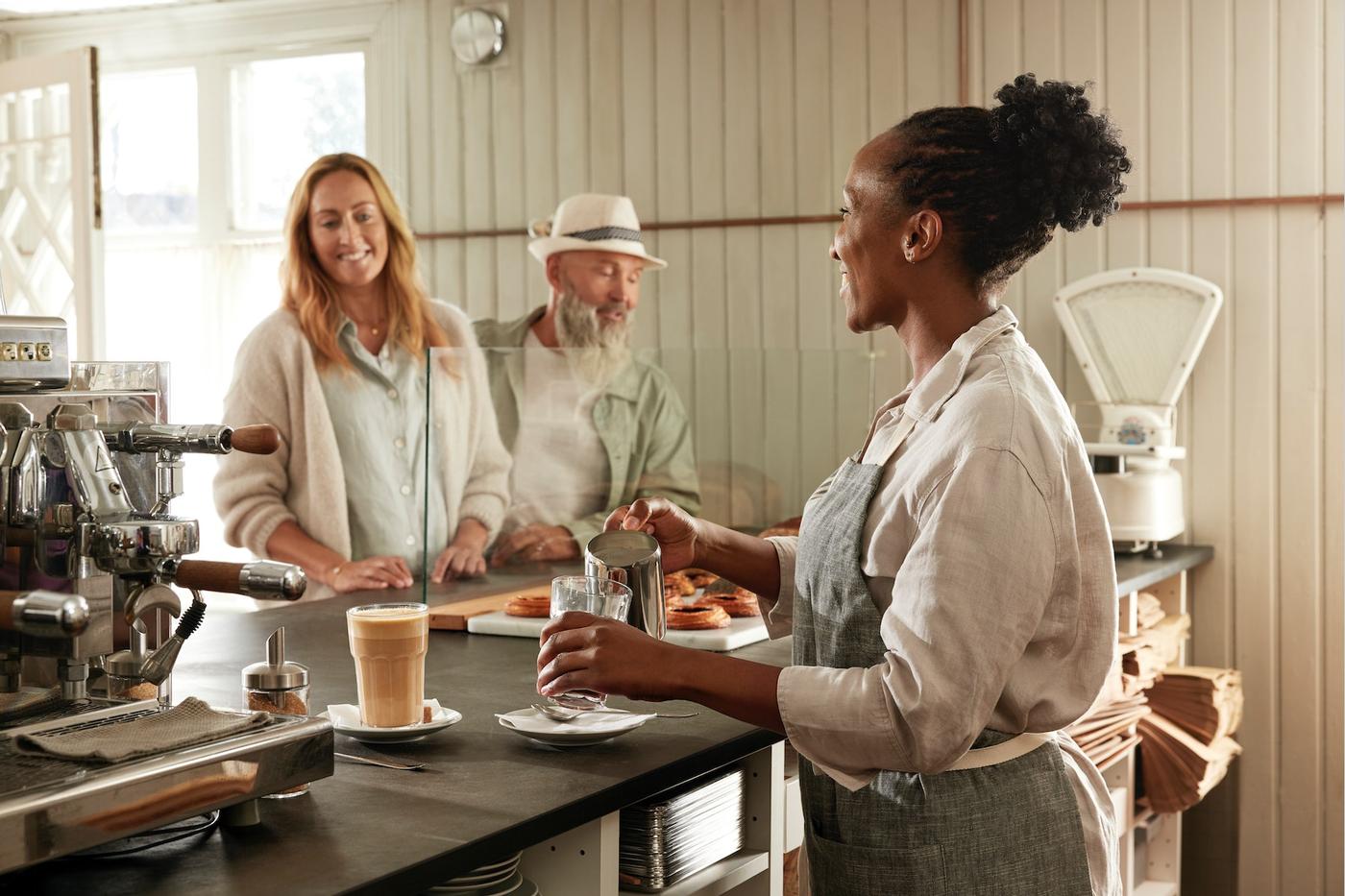 Une barista sert un café à une cliente derrière un comptoir.