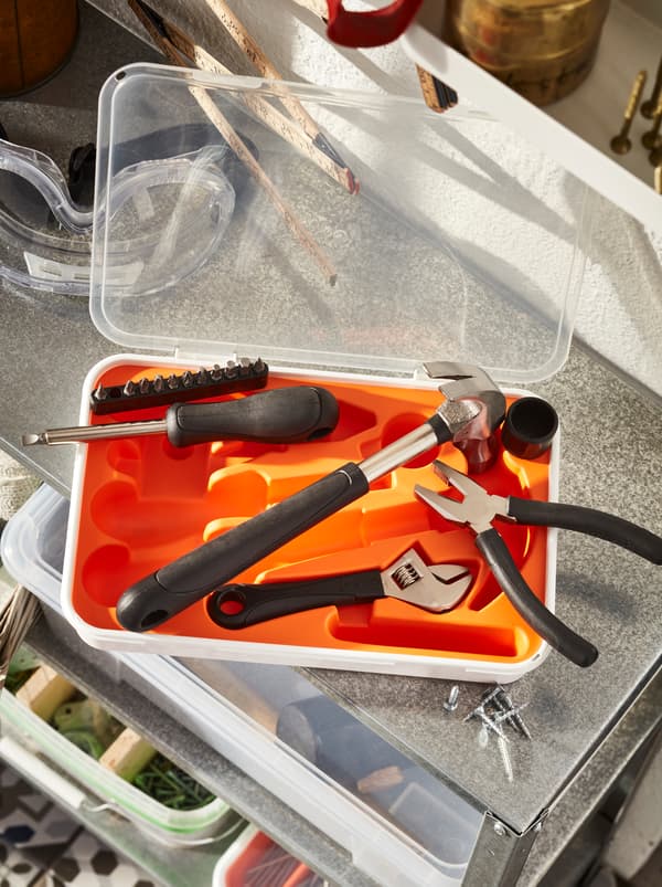 Une boîte à outils FIXA ouverte, certains des outils à l’extérieur, sur le dessus d’une armoire en métal à tablettes ouvertes contenant des boîtes et des accessoires de bricolage pour la maison.