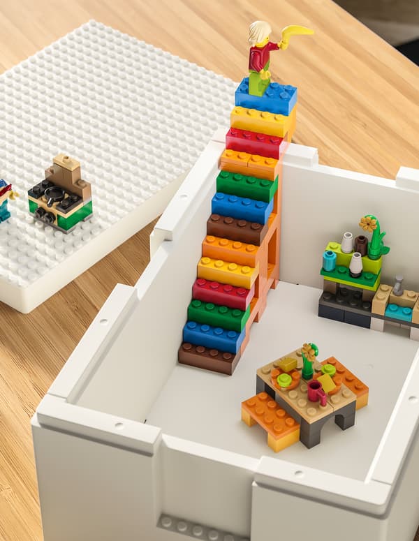 Une boîte BYGGLEK blanche contenant des constructions LEGO et un escalier aux couleurs vives sur une table.