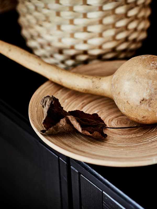Une calebasse séchée et une feuille flétrie reposent dans un plat HULTET en bambou posé sur une surface en bois foncé.
