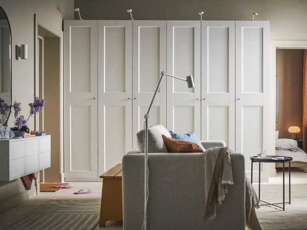 Une causeuse-lit VIMLE beige au milieu d’une chambre et deux armoires-penderies PAX/GRIMO blanches contre un mur noir.