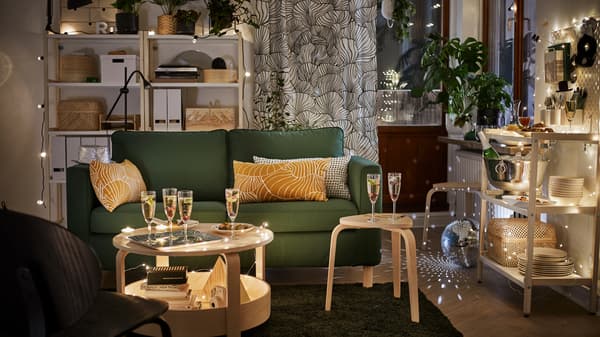 Une causeuse PÄRUP vert foncé dans un salon avec des flûtes à champagne et des guirlandes lumineuses.