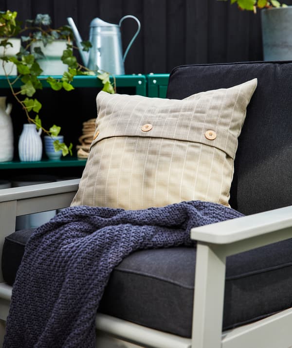 Une chaise d’extérieur avec des coussins bleu foncé et un oreiller supplémentaire beige sur une couverture bleu foncé.
