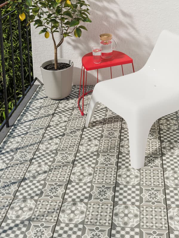 Une chaise d’extérieur en plastique blanc avec une table d’extérieur rouge et une plante dans un cache-pot sur un balcon avec un revêtement de sol à motifs.