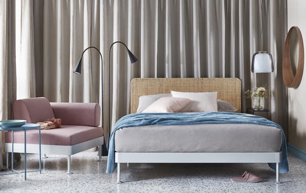 Une chambre à coucher aux tons neutres doux gris, beige et rose avec un lit double, un lampadaire, un fauteuil et une table d’appoint.