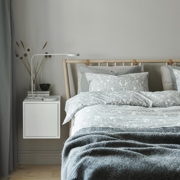 Une chambre à coucher avec du linge de lit dans les tons neutres et une table de chevet fixée à un mur blanc.