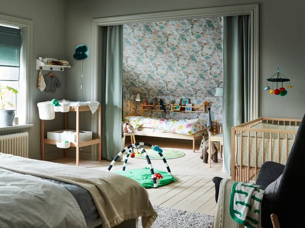 Une chambre à coucher avec un lit double, une table à langer et des accessoires pour bébé. Un lit bébé installé dans une alcôve derrière des rideaux verts.