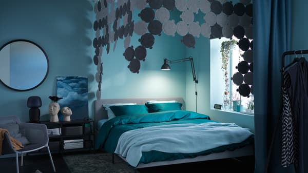 Une chambre à coucher avec un lit SLATTUM installé près d’une fenêtre. Au-dessus du lit se trouve un ciel de lit créé en panneaux acoustiques ODDLAUG.