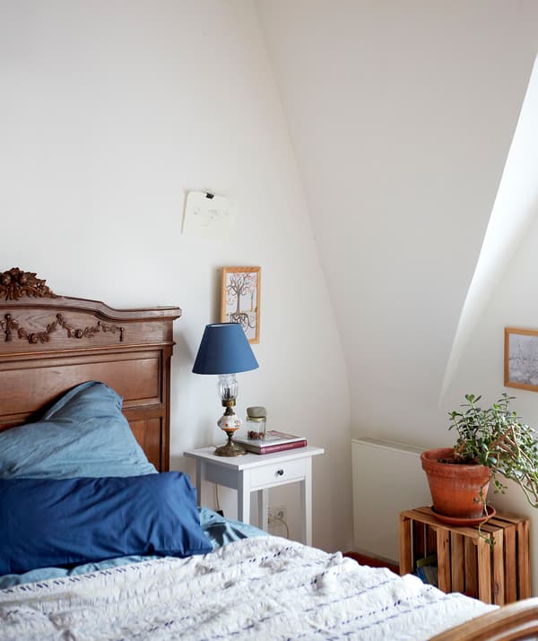 Une chambre à coucher avec un toit en pente, un lit en bois foncé avec du linge de lit bleu et une table de chevet blanche.