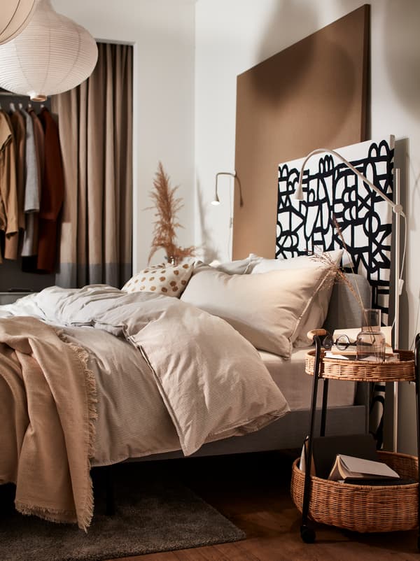 Une chambre à coucher avec une structure de lit matelassée grise SLATTUM ainsi que des housses de couette et des taies d’oreiller beiges BERGPALM.