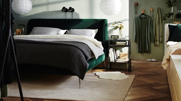 Une chambre à coucher avec une structure de lit matelassée TUFJORD vert foncé, deux suspensions avec abat-jour, une literie blanche et un couvre-lit gris.