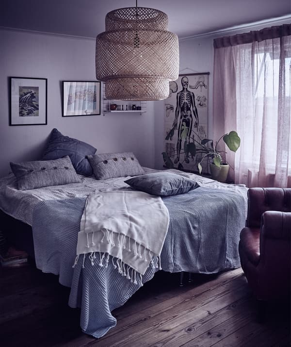 Une chambre à coucher cosy avec des murs gris, des coussins bleus et gris, des plaids sur le lit et des suspensions en rotin.