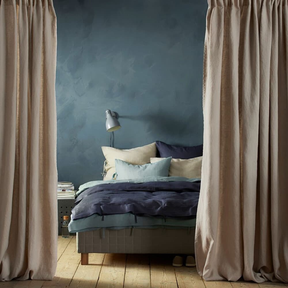 Une chambre à coucher divisée en deux grâce à deux rideaux beige.