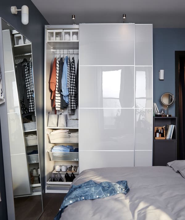 Une chambre avec, contre le mur, une petite armoire étroite jouxtant une garde-robe PAX, porte coulissante ouverte montrant un contenu organisé.
