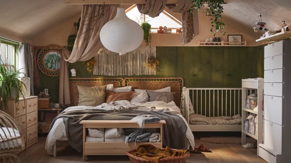 Une chambre boho avec un lit deux places recouvert de linge de lit neutre et de coussins, avec un lit à barreaux GULLIVER blanc à côté.