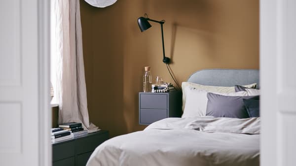 Une chambre confortable avec des murs couleur caramel et un cadre de lit matelassée VADHEIM, une applique et une table de chevet.