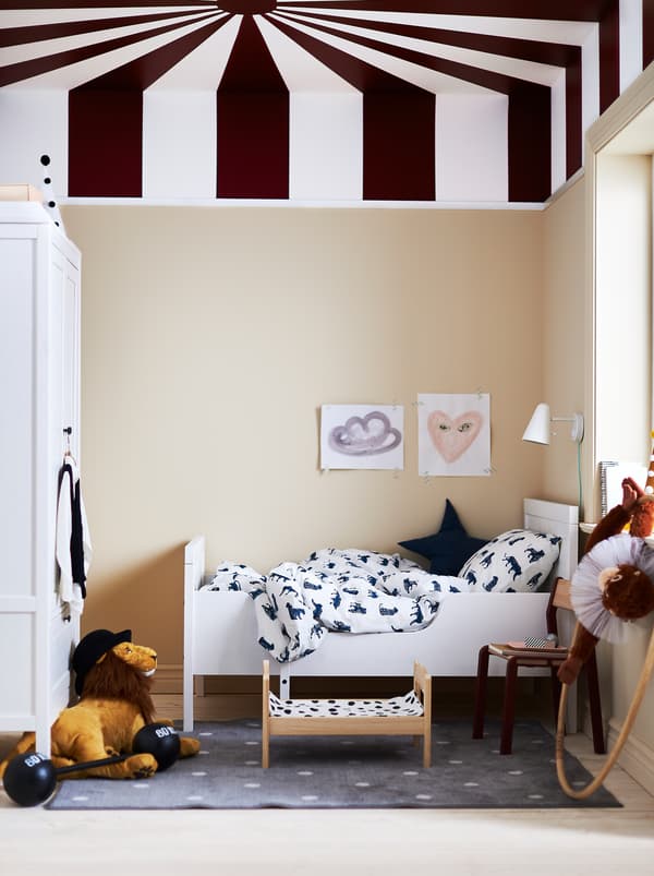 Une chambre d’enfant au plafond rappelant un chapiteau de cirque, un lit extensible SUNDVIK blanc et du linge de lit blanc et bleu foncé.