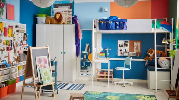 Une chambre d’enfant avec un lit mezzanine VITVAL blanc sous lequel est installé un bureau encastrable, un chevalet MÅLA et beaucoup de rangement.
