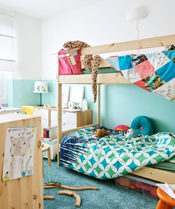 Une chambre d’enfant en blanc et turquoise. Des lits superposés en bois avec du linge de lit, des commodes en blanc et bois, et un tapis turquoise.