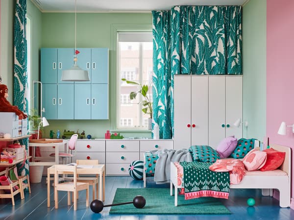 Une chambre d’enfants avec armoires et commodes blanches, deux cadres de lit extensibles, un tapis vert et armoires murales bleues.