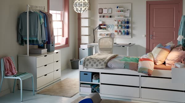 Une chambre d’étudiant pastel avec en vedette un lit intégrant des tiroirs, non loin d’un bureau et d’un rangement pour vêtements suspendus.