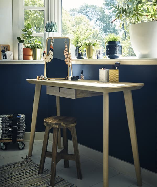 Une coiffeuse et un tabouret sous une fenêtre et contre un mur bleu.