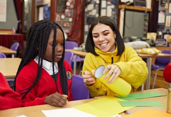 Une collaboratrice IKEA aide une enfant en uniforme scolaire pour un bricolage avec du papier coloré.