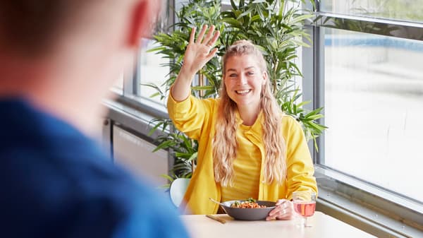 Une collaboratrice IKEA vêtue d’un uniforme jaune qui envoie la main à un collègue dans la cantine du personnel.