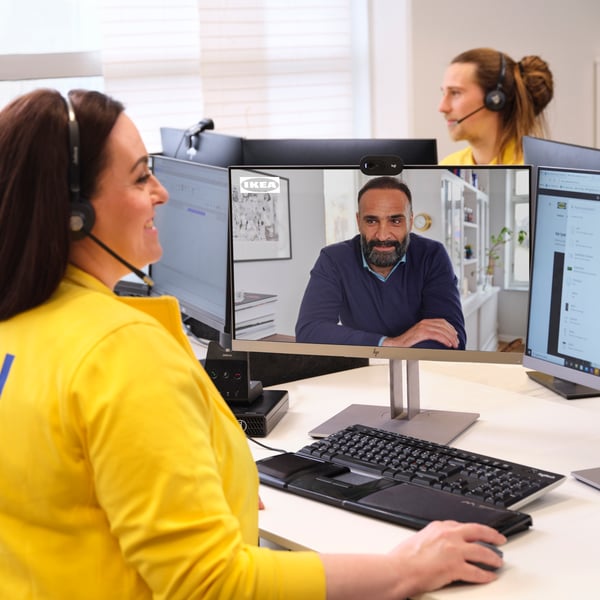 Une collaboratrice portant un uniforme jaune est assise à un bureau et discute avec un client lors d’un appel virtuel.
