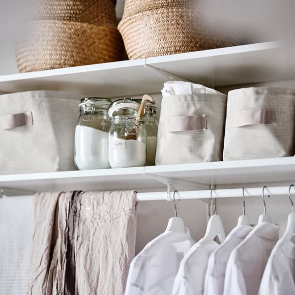 Une combinaison d’armoire-penderie blanche avec des paniers en jonc de mer, des paniers en tissu beige et des vêtements sur des cintres blancs.