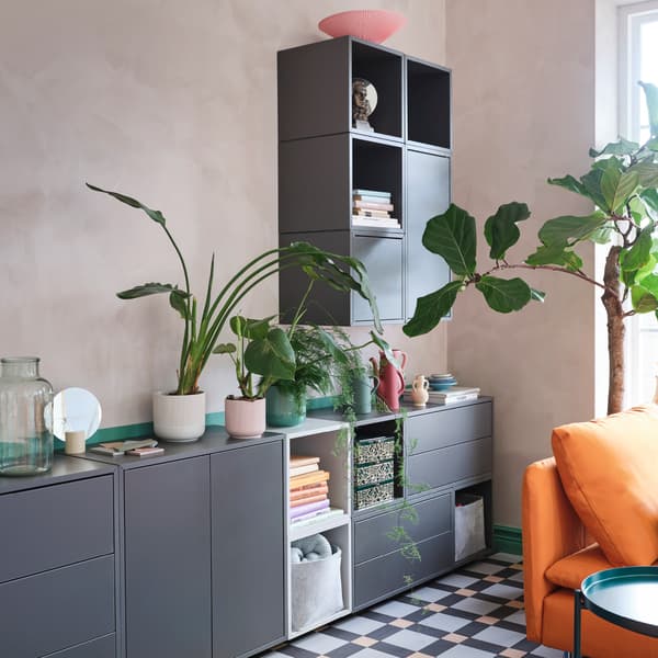 Une combinaison d’armoires grises et vertes avec des tablettes, des tiroirs et des portes, dans un espace avec plusieurs plantes vertes.