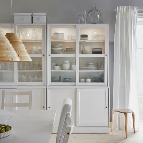 Une combinaison de rangement blanche HAVSTA avec des portes en verre coulissantes dévoilant de la vaisselle et des verres dans une salle à manger.