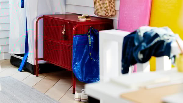 Une commode NIKKEBY rouge entourée de divers accessoires typiques d’une entrée, dans une pièce lambrissée de blanc.