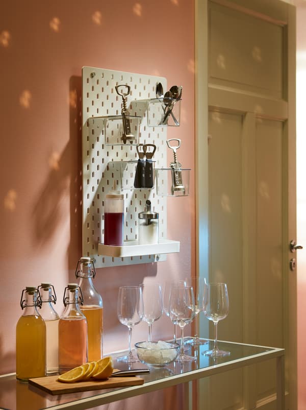 Une coupe de bienvenue est servie sur une table basse. Des tire-bouchons IDEALISK et d’autres accessoires sont présentés sur un panneau perforé SKÅDIS.