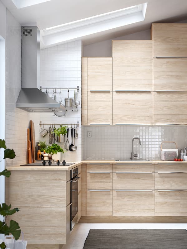 Une cuisine avec des armoires IKEA SEKTION dotées de portes et façades ASKERSUND à effet frêne clair et une hotte aspirante en acier inoxydable.