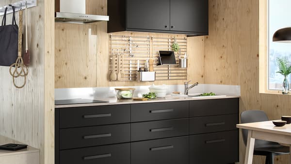 Une cuisine avec des portes d’armoire et façades de tiroirs KUNGSBACKA anthracite, un plan de travail blanc à effet minéral/paillettes et des murs en bois.