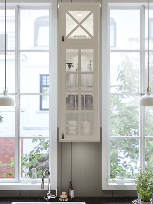 Une cuisine avec une armoire étroite blanc cassé à porte vitrée entre deux fenêtres et un plan de travail à effet minéral noir.