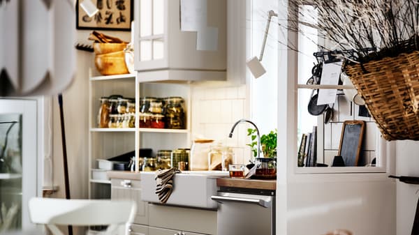 Une cuisine beige au style rustique avec une armoire STENSUND, un évier blanc et des étagères ouvertes et fermées où sont rangés des pots et des ustensiles.