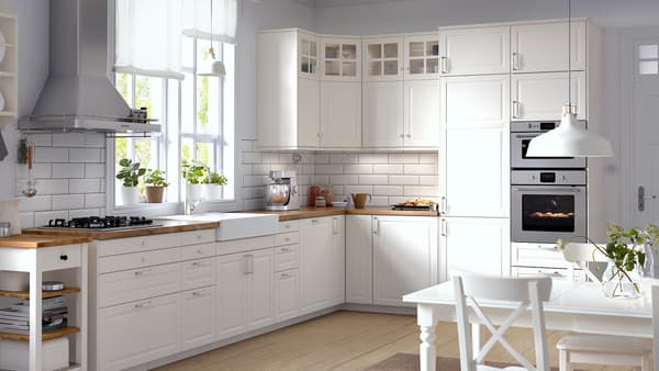 Une cuisine d’angle avec des portes BODBYN et des faces de tiroirs blanc cassé, ainsi que des portes vitrées à croisillons.