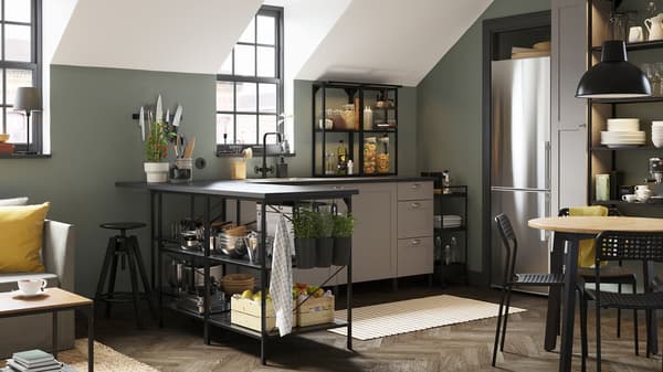 Une cuisine d’angle gris/anthracite avec une desserte noire, un tapis rayé et des récipients noirs contenant des herbes fraîches.