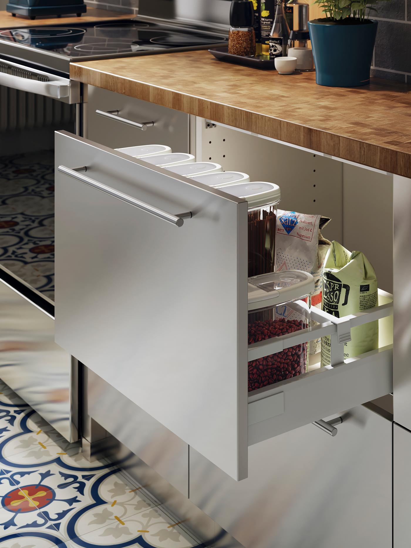 Une cuisine en acier inoxydable avec un comptoir en chêne et placage. Un tiroir est ouvert et des aliments secs sont rangés à l’intérieur.
